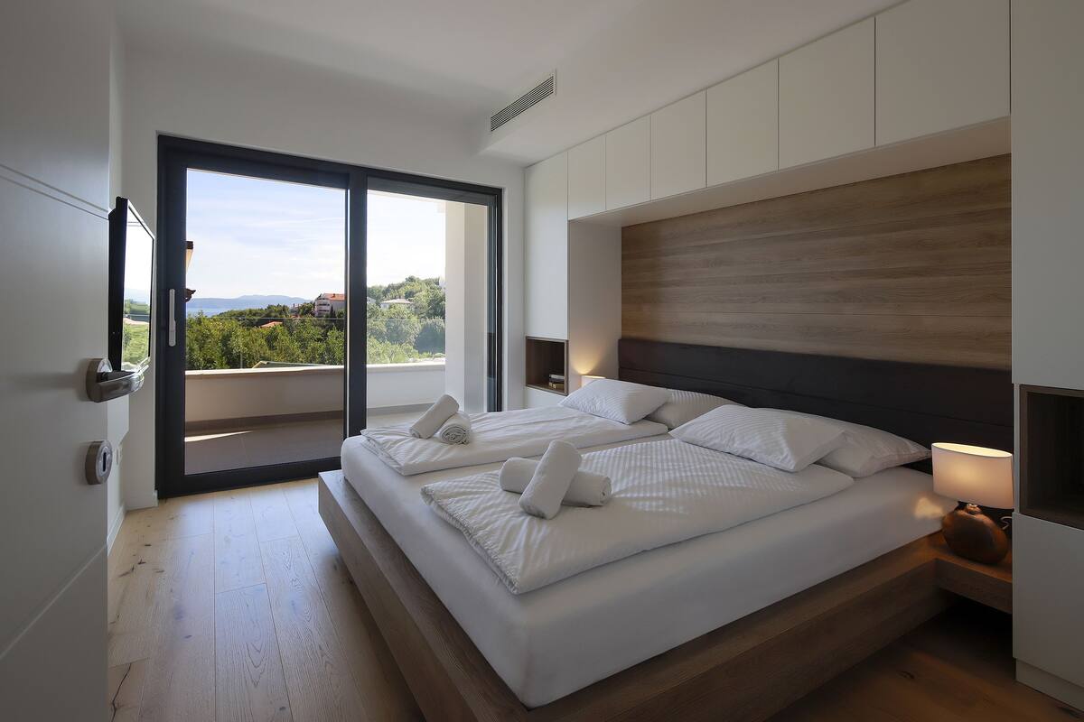 A modern bedroom with two beds, a large sliding glass door leading to a balcony, and a minimalist design.