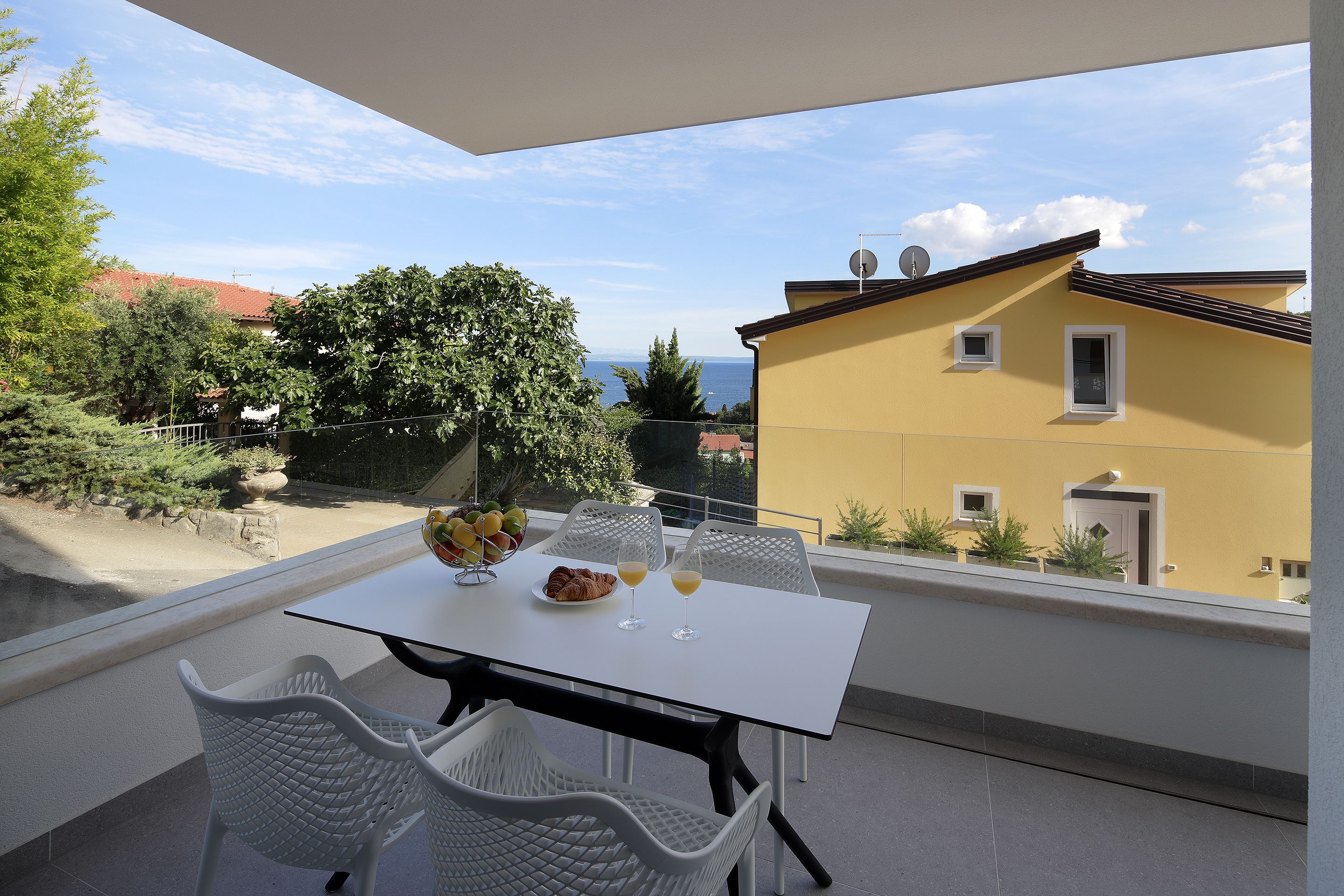 A balcony with a table set for two, overlooking a scenic view of the sea and a yellow building.