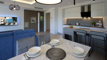 Un comedor moderno con una mesa blanca preparada para cuatro comensales, un sofá azul y una cocina con un televisor de pantalla plana sobre la encimera.