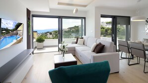A modern living room with a large TV, a teal armchair, a white sofa, and a dining area with a table and chairs. - Modena Maris Apartments (Opatija)