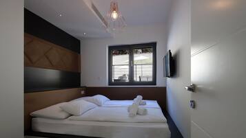 Une chambre moderne avec un grand lit, une tête de lit, une fenêtre avec des stores et un téléviseur fixé au mur.