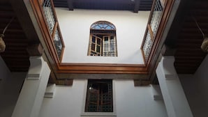 Une pièce avec un plafond haut, une petite fenêtre ornée d’un cadre décoratif et un escalier en bois.