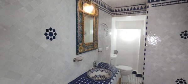 A bathroom with a white sink, a mirror with a decorative frame, and patterned tiles on the walls and floor.