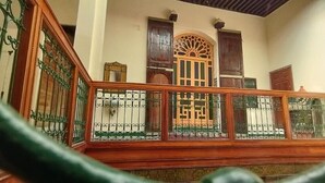 Un escalier avec une rampe en bois et des barreaux en métal, menant à une pièce dotée d’une porte et d’une fenêtre en bois.