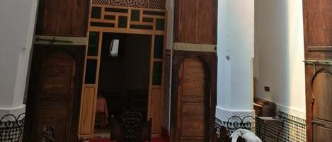 Um interior tradicional marroquino com uma mesa de jantar de madeira, cadeiras e um arco decorativo.
