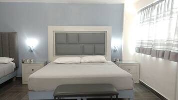 A modern bedroom with a large bed, bedside tables, a bench, and a window with curtains.