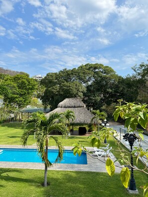 A swimming pool surrounded by lush greenery, a thatched-roof structure, and a clear blue sky. - Hotel Suite Las Valkirias (Santa María Huatulco)