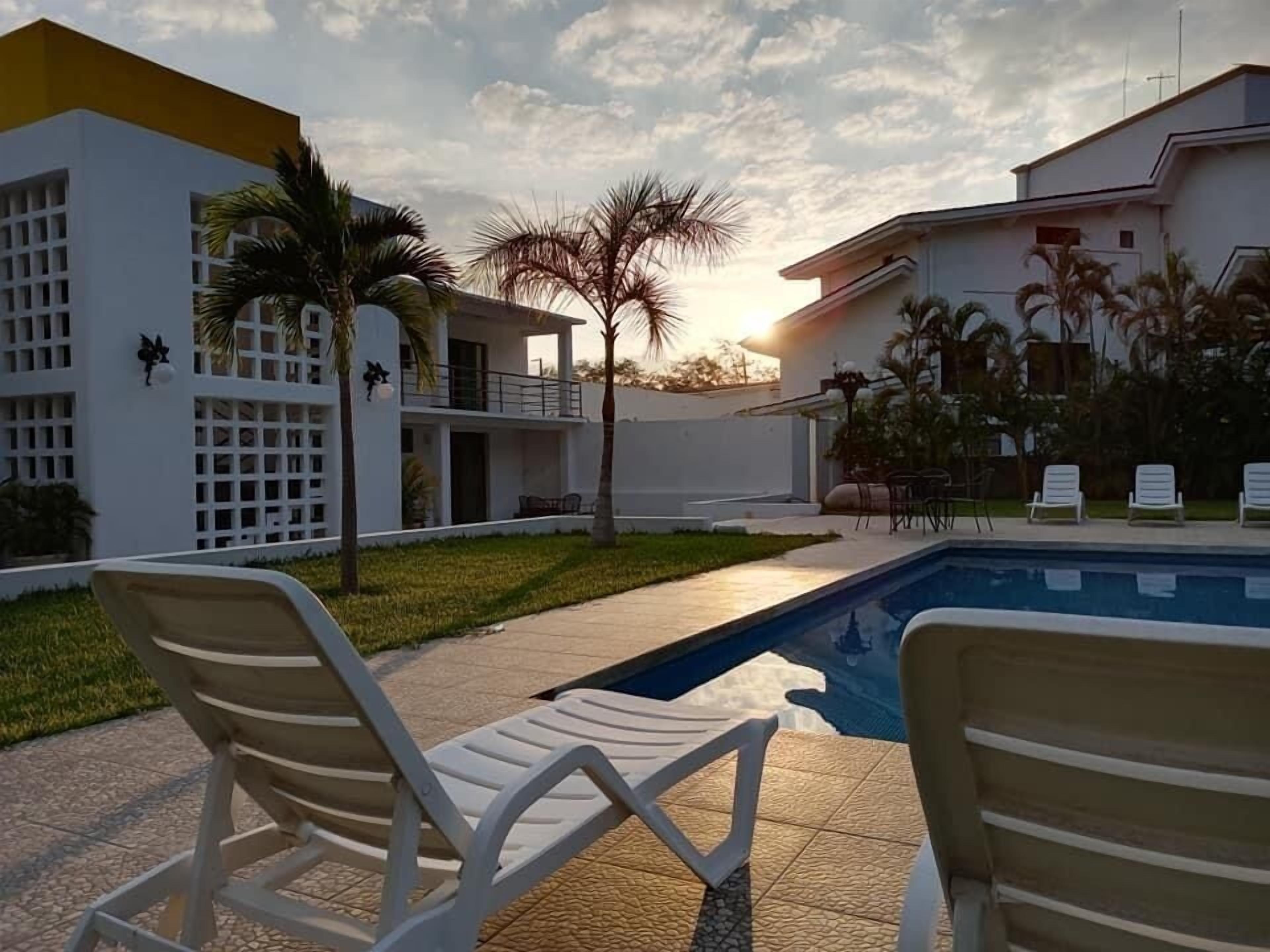 Zona junto a la piscina con sillones de descanso, una piscina y un edificio con fachada blanca y balcones.