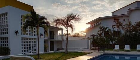 Zona junto a la piscina con sillones de descanso, una piscina y un edificio con fachada blanca y balcones.