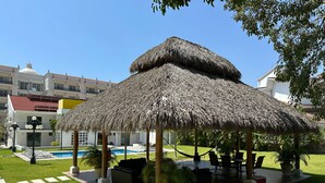 Ein Gazebo mit Strohdach, Außenbereich, Pool und gepflegtem Rasen.