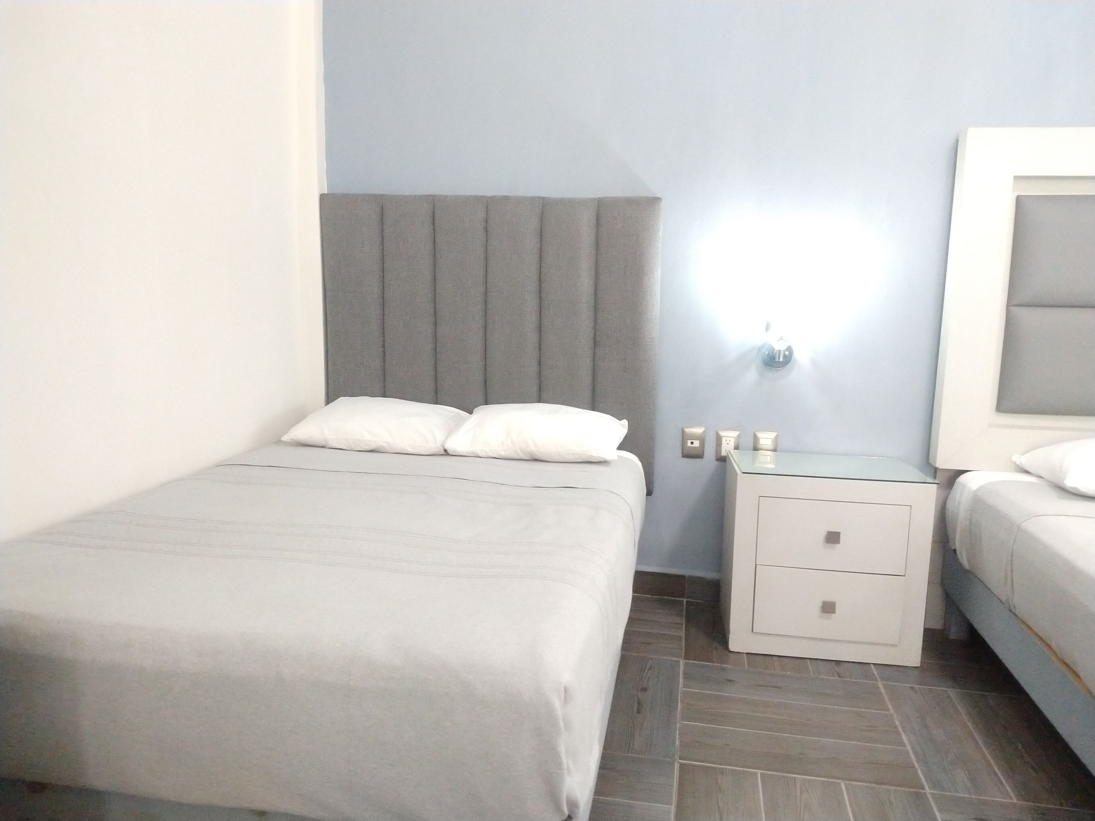 Une chambre d’hôtel avec un lit simple, une table de chevet avec une lampe et une petite table d’appoint.