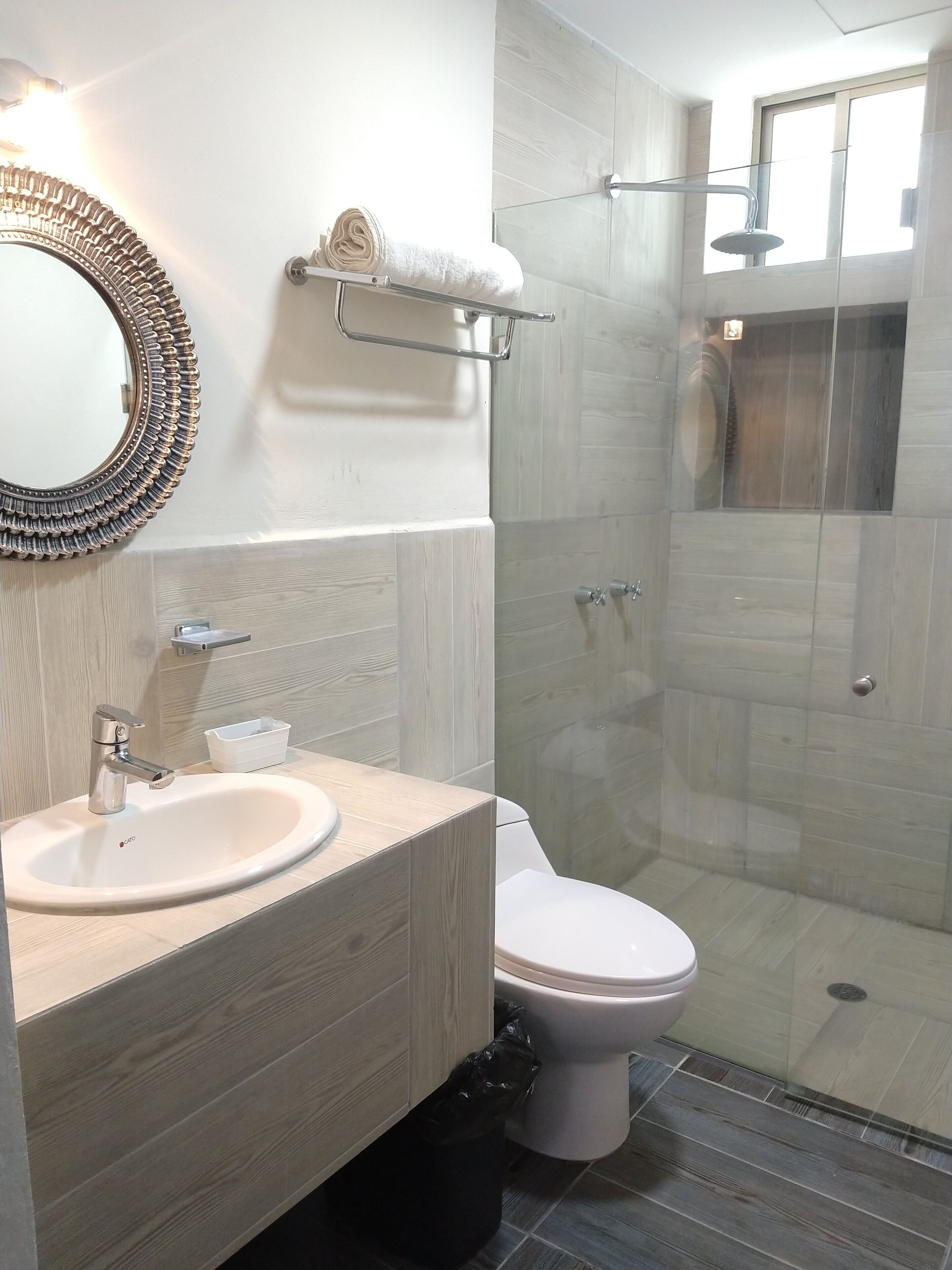 Un baño moderno con tocador de madera, espejo redondo, inodoro y cabina de ducha con vidrio.