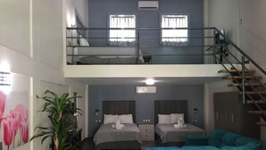 Ein Hotelzimmer mit zwei Stockwerken, einem Balkon, einer Treppe, einem Bett mit einem schwanenförmigen Kopfkissen, einer Couch und einer Topfpflanze.