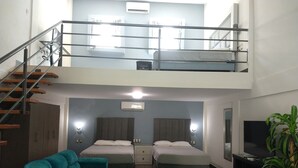 Un appartement à deux étages avec un escalier, un canapé, un lit, une télévision et une plante en pot.