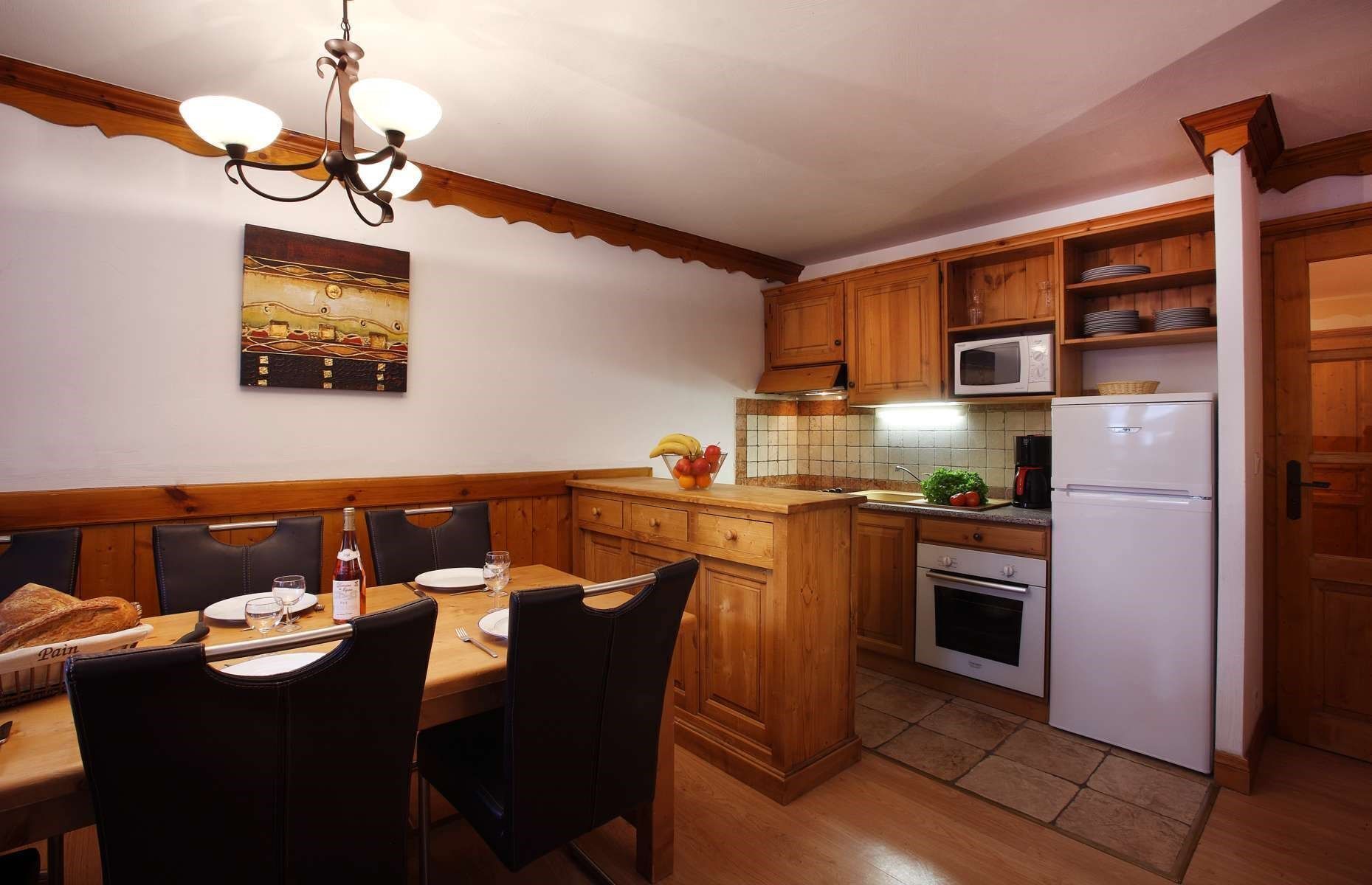 A compact kitchen with wooden cabinets, a microwave, an oven, and a dining area with a table set for two.