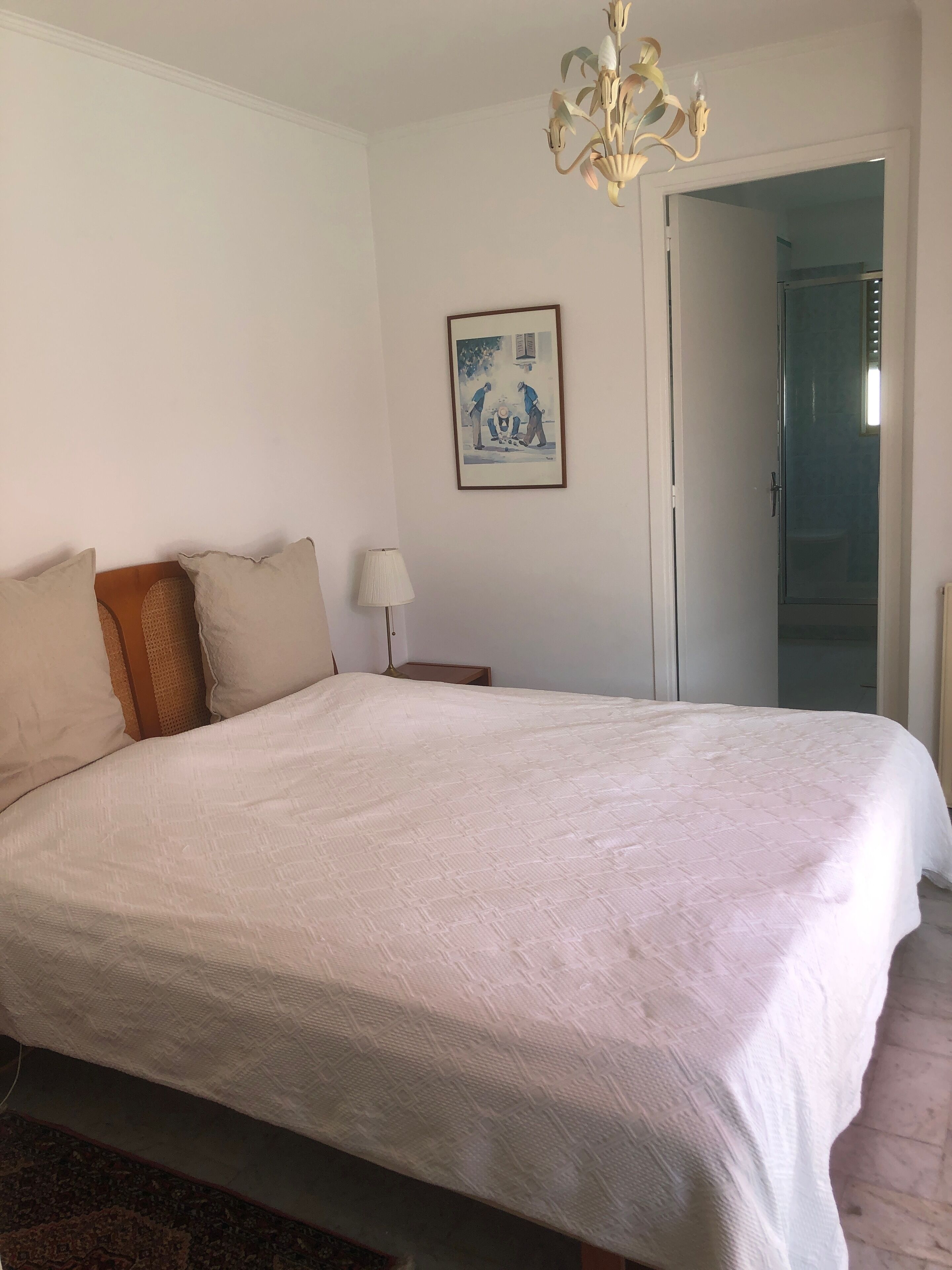 A large bed with a white duvet, a floor lamp, and a painting on the wall.