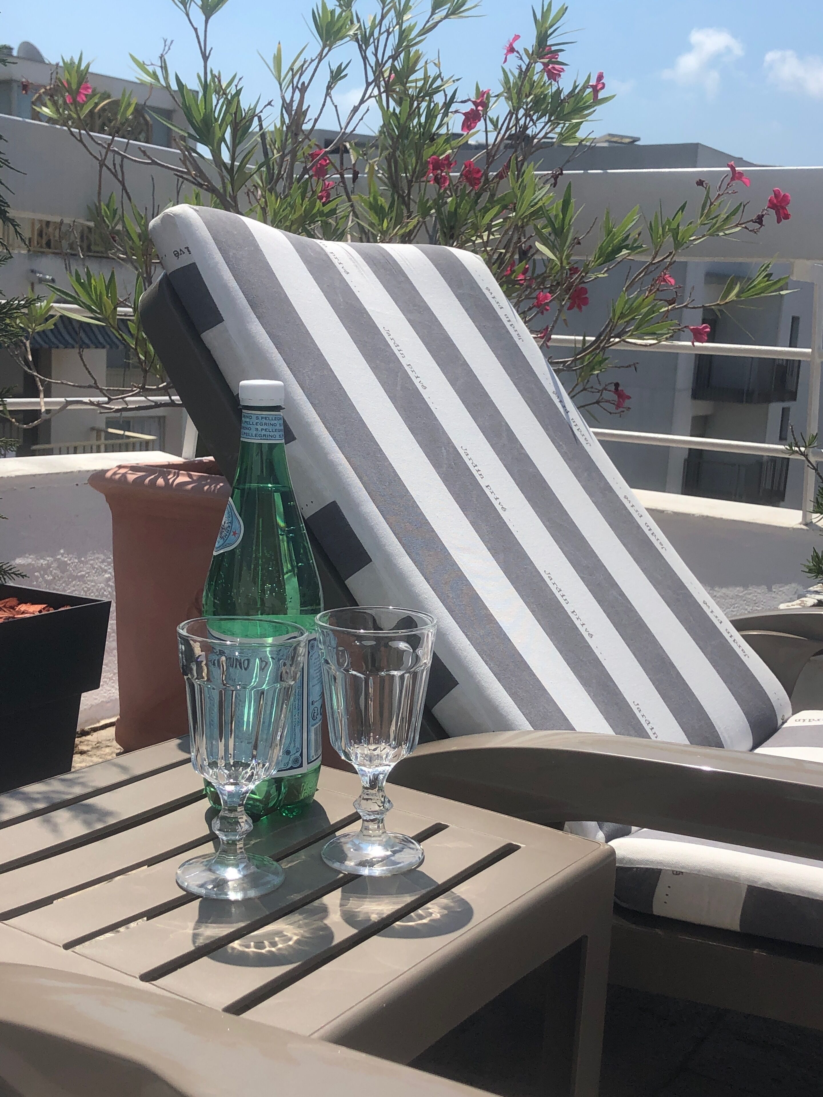 A table with a striped lounge chair, a bottle of water, and two glasses.