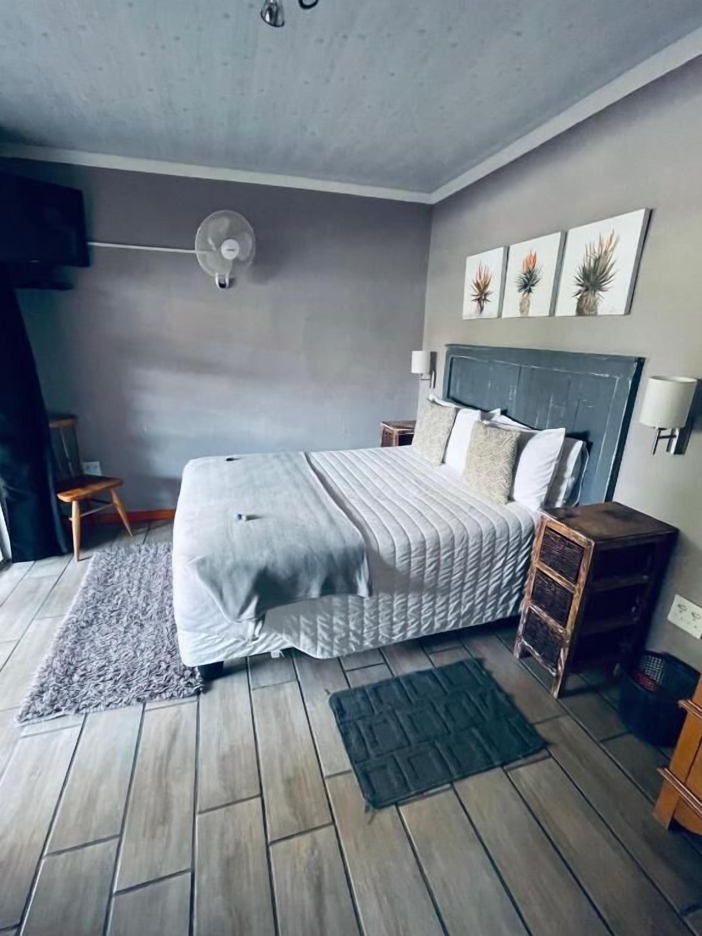 A bedroom with a bed, bedside tables, a floor lamp, a fan, and artwork on the wall.
