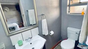 Casa de banho com lavatório branco, espelho, sanita e janela.
