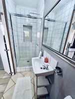 A bathroom with a glass-enclosed shower, a white sink, and a mirror.