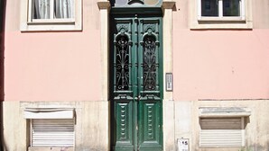 A building facade with a green double door, two windows with shutters, and two closed shutters below the door.