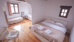 Un dormitorio con una cama grande, una silla, una mesita y un ventanal.