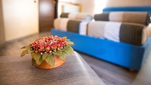 Une pièce avec un lit en arrière-plan, une petite table sur laquelle se trouve un objet décoratif, et un plancher en bois.