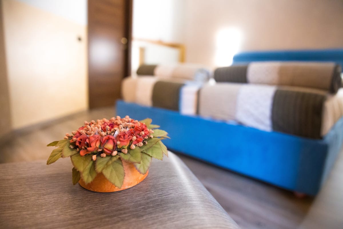 Ein Zimmer mit einem Bett im Hintergrund, einem kleinen Tisch mit einer Dekoration und einem Holzboden.