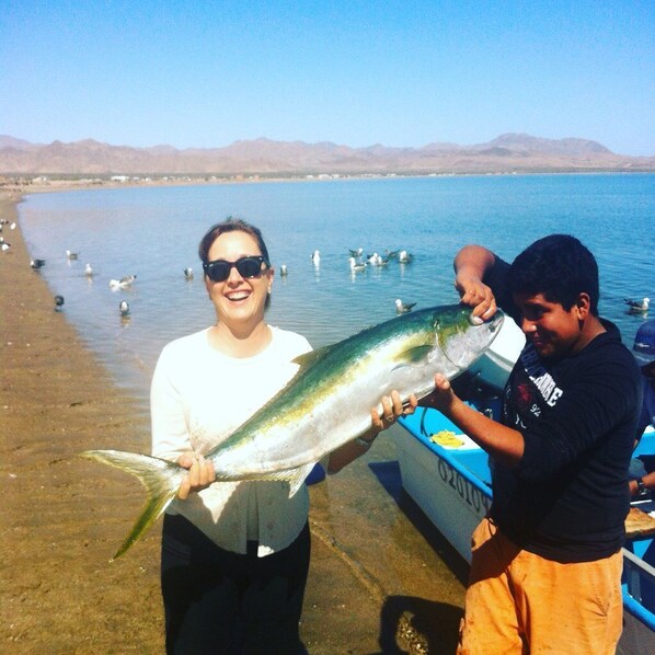 Dos personas sostienen un pez grande junto a un lago con montañas al fondo.