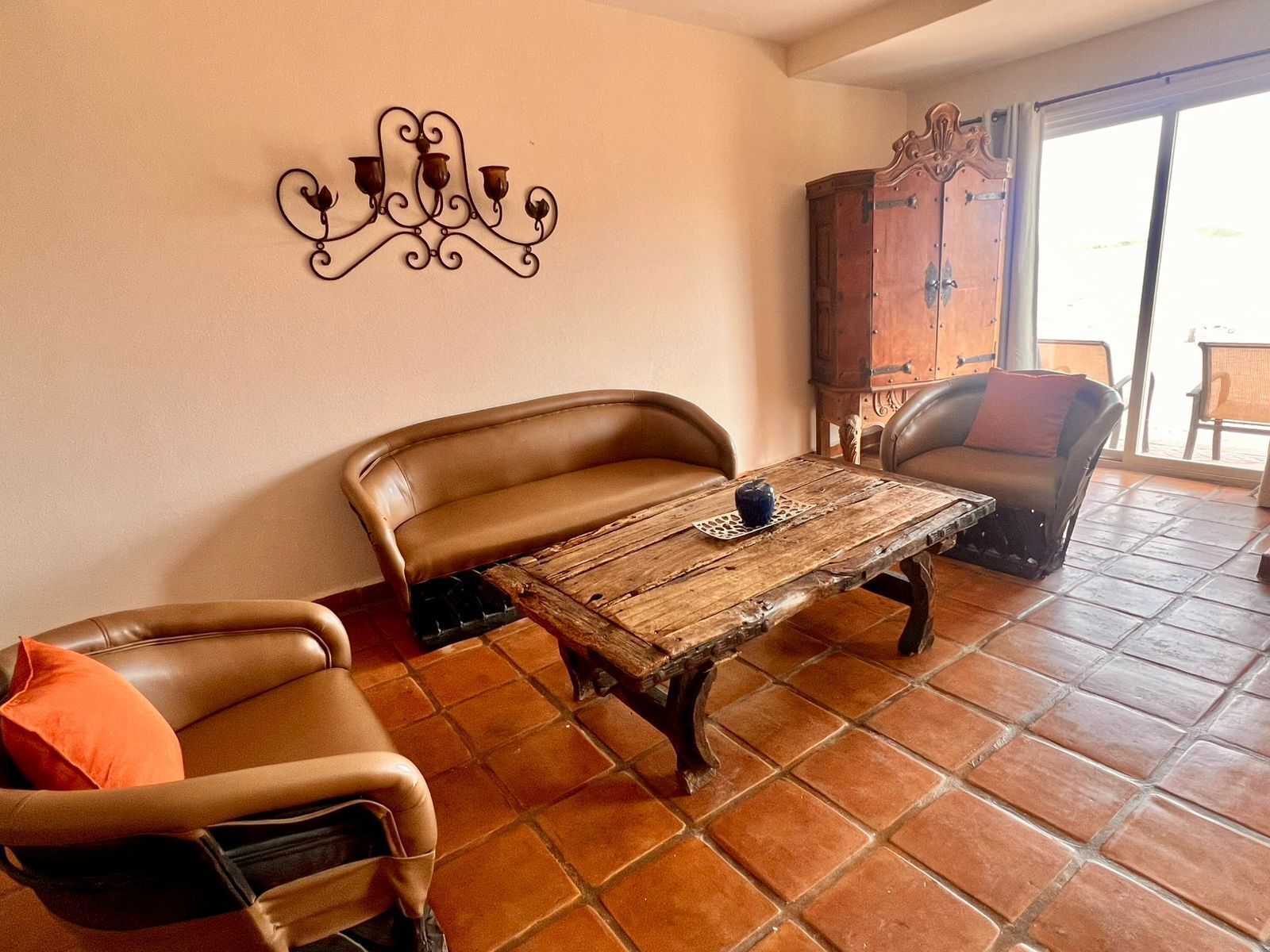 A living room with a brown leather sofa, a wooden coffee table, and a brown leather armchair. There is a decorative metal wall piece above the sofa.
