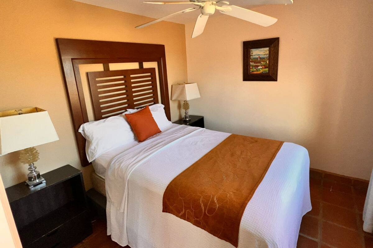 A neatly made bed with a white and brown blanket, a wooden headboard, and a ceiling fan.