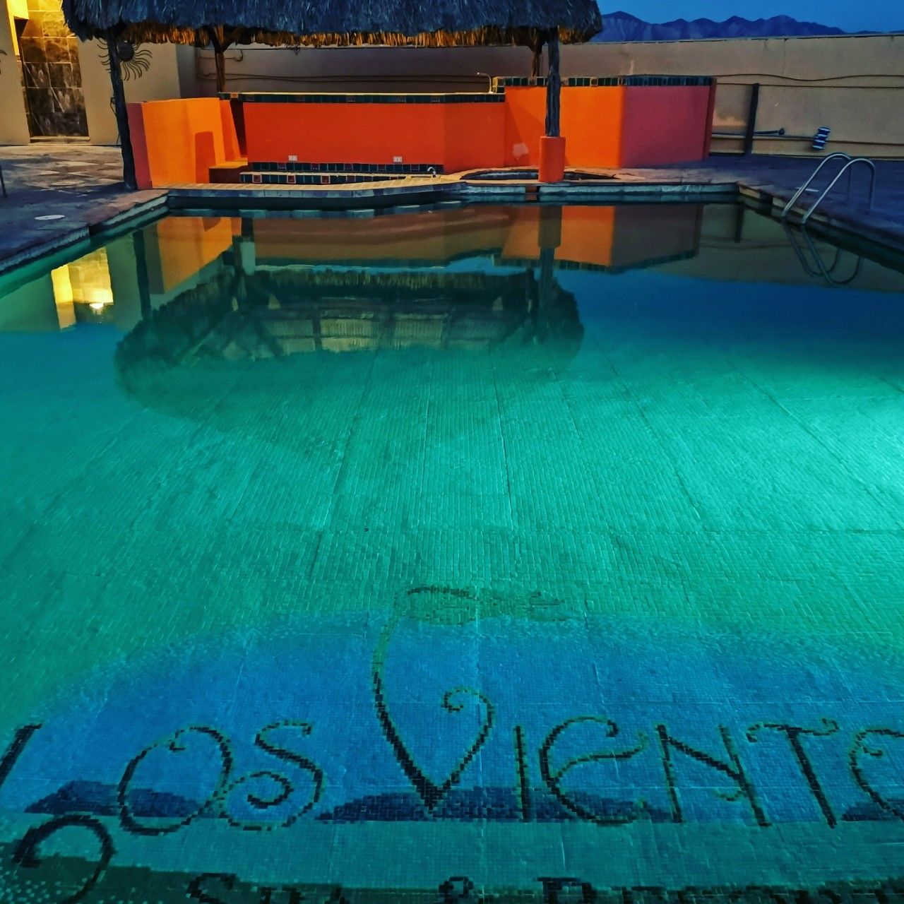 A swimming pool with a thatched roof structure and a sign reading "Los Vientos".