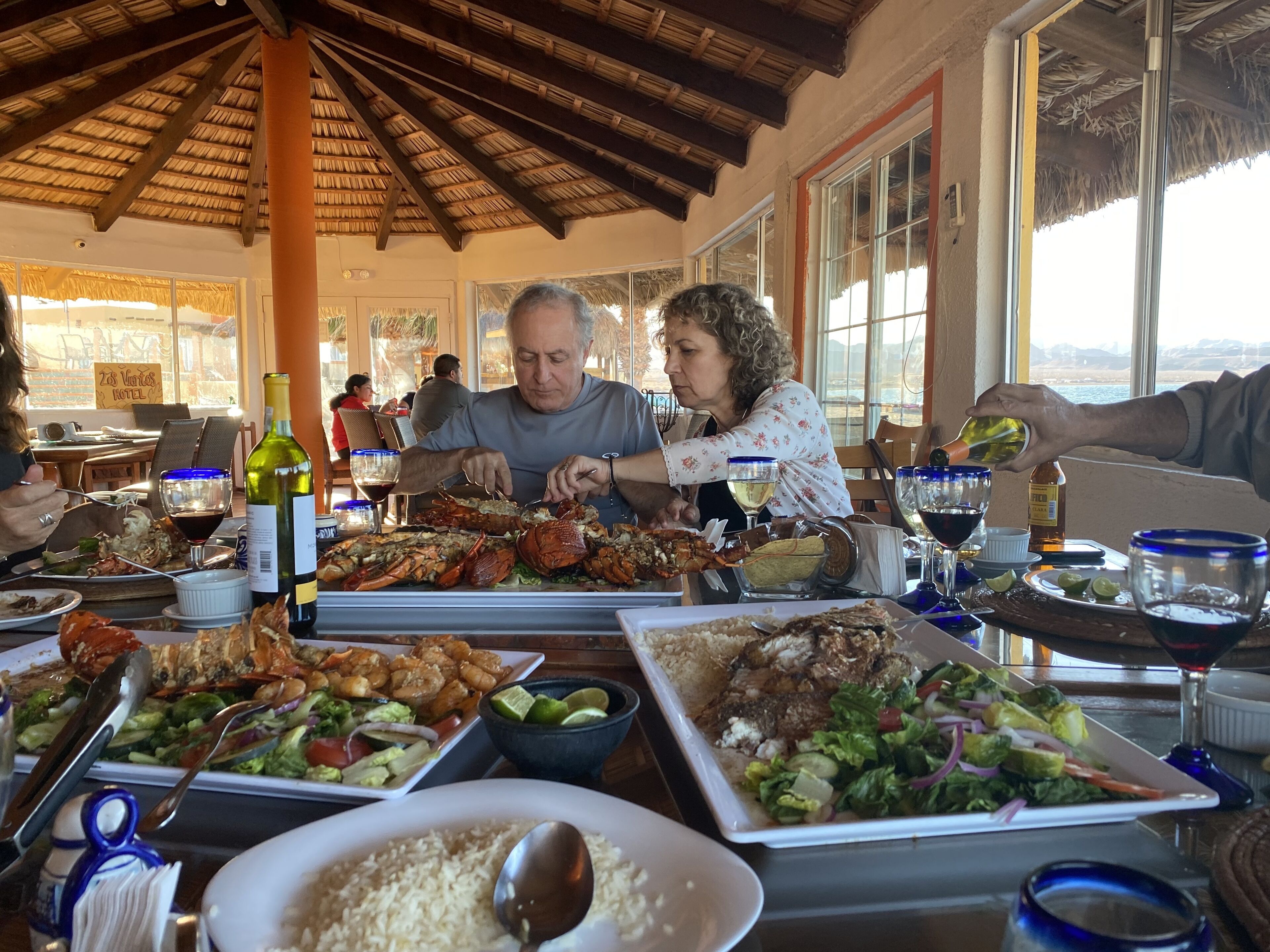 A restaurant with a thatched roof, large windows, and a variety of dishes on the table.