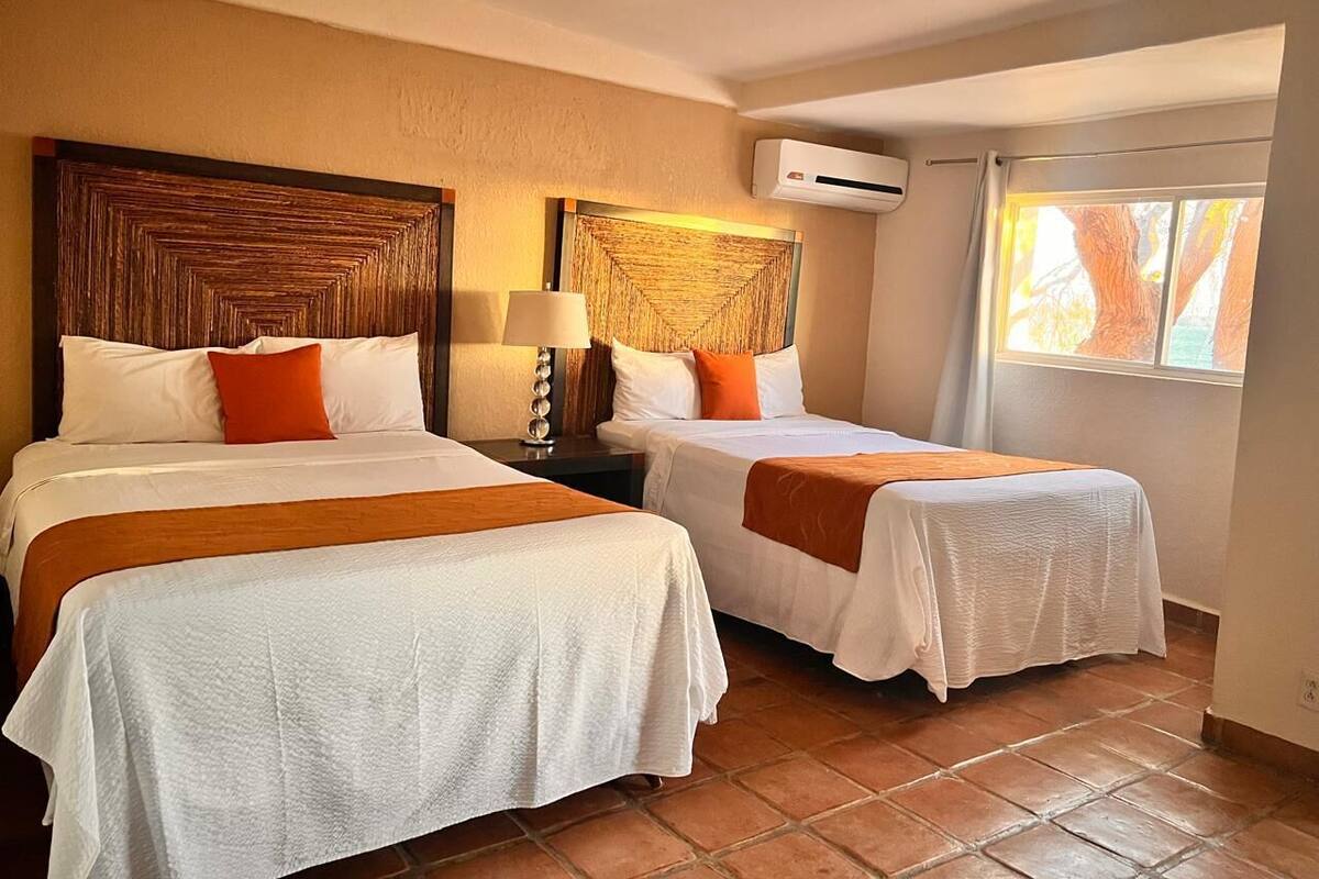 A hotel room with two beds, a wooden headboard, a window with curtains, and an air conditioning unit.