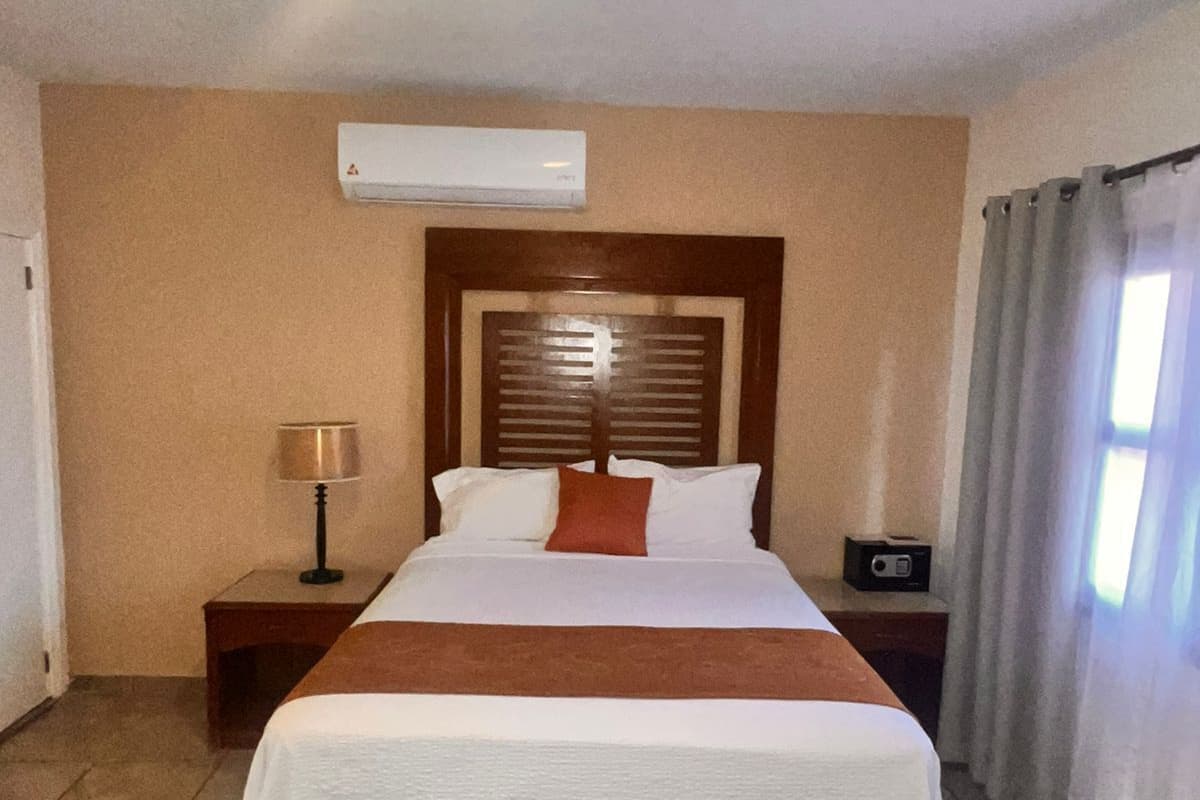 A hotel room with a bed, a nightstand, a lamp, an air conditioning unit, and a radio.