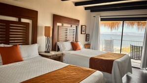 A hotel room with two beds, a nightstand, a lamp, a window with a view of the sea, and a balcony with a railing. - Los Vientos Hotel (Bahia de los Angeles)