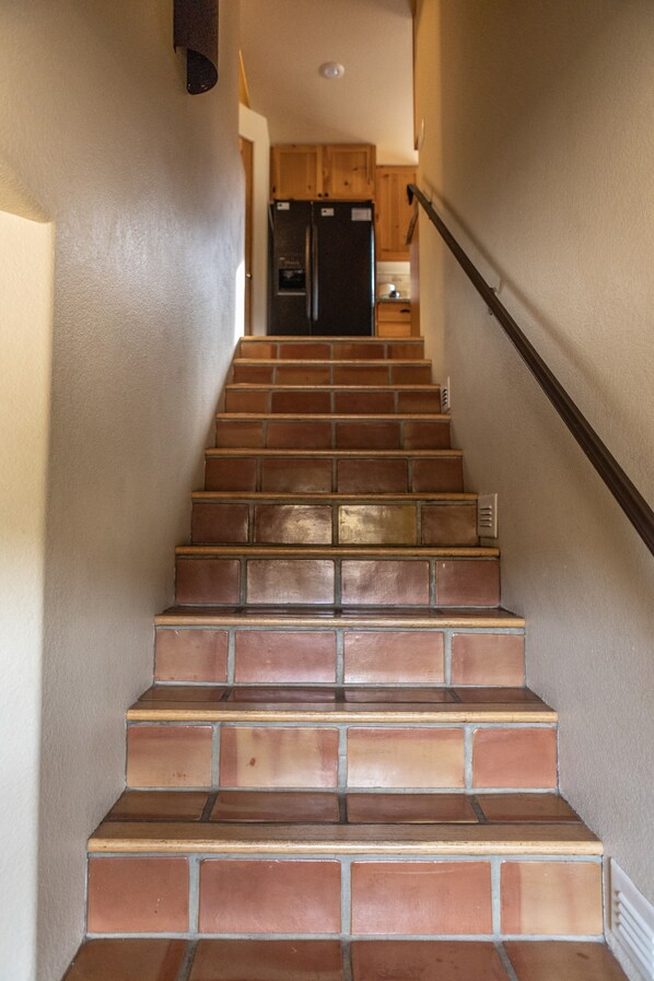 Un escalier recouvert de carreaux bruns mène à une cuisine équipée de meubles en bois et d’un réfrigérateur noir.