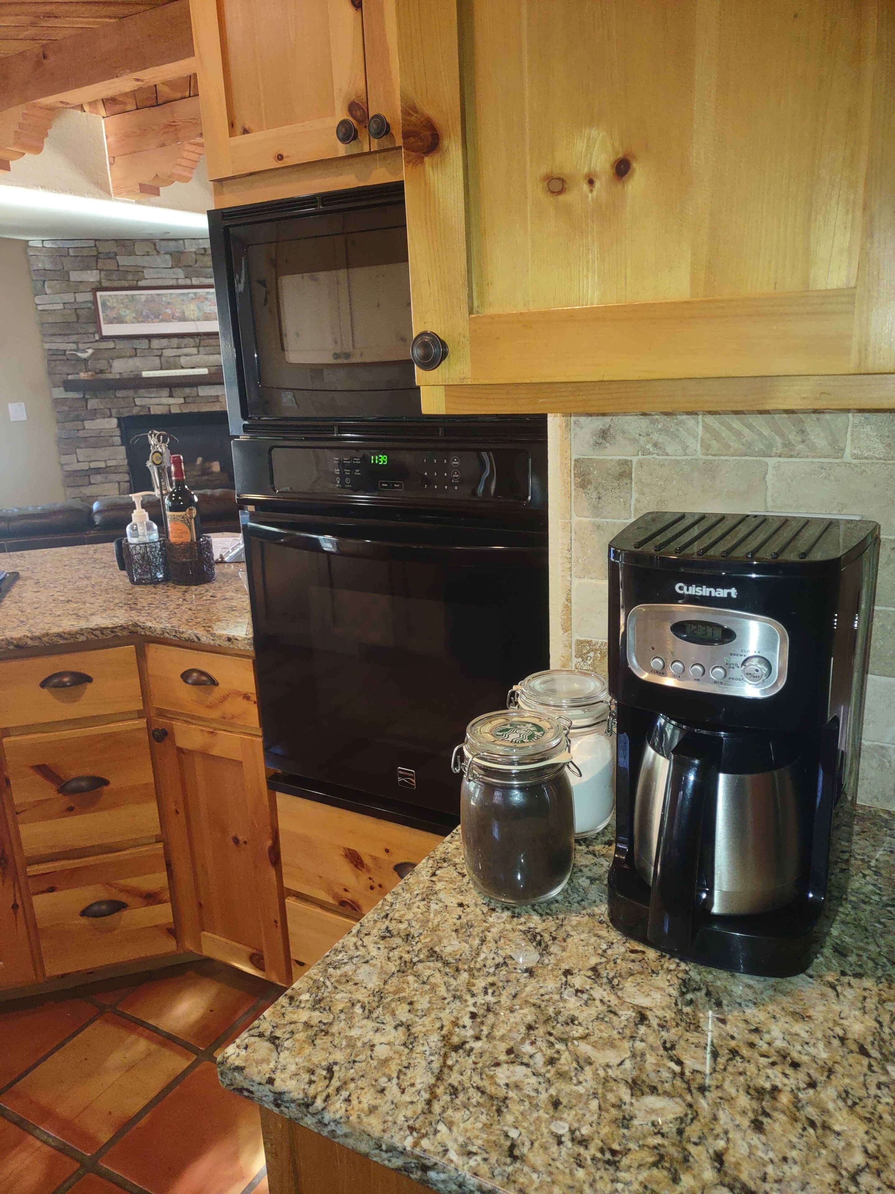 A kitchen with wooden cabinets, a black oven, a coffee maker, and a stone backsplash.