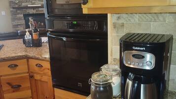 A kitchen with wooden cabinets, a black oven, a coffee maker, and a stone backsplash.