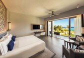 A hotel room with a bed, desk, TV, and a balcony with a view of the ocean.
