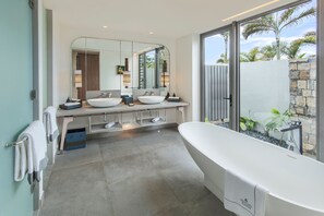 A modern bathroom with a freestanding bathtub, two sinks, and a large mirror.