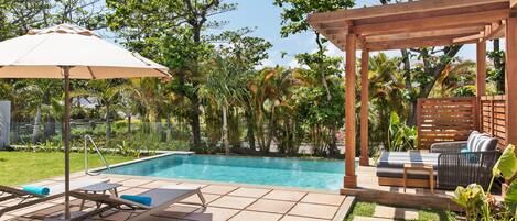 A pool area with tiled flooring, lounge chairs, and a pergola with seating.