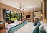 A spacious bedroom with a large bed, a ceiling fan, a TV mounted on the wall, and a view of the outdoors.