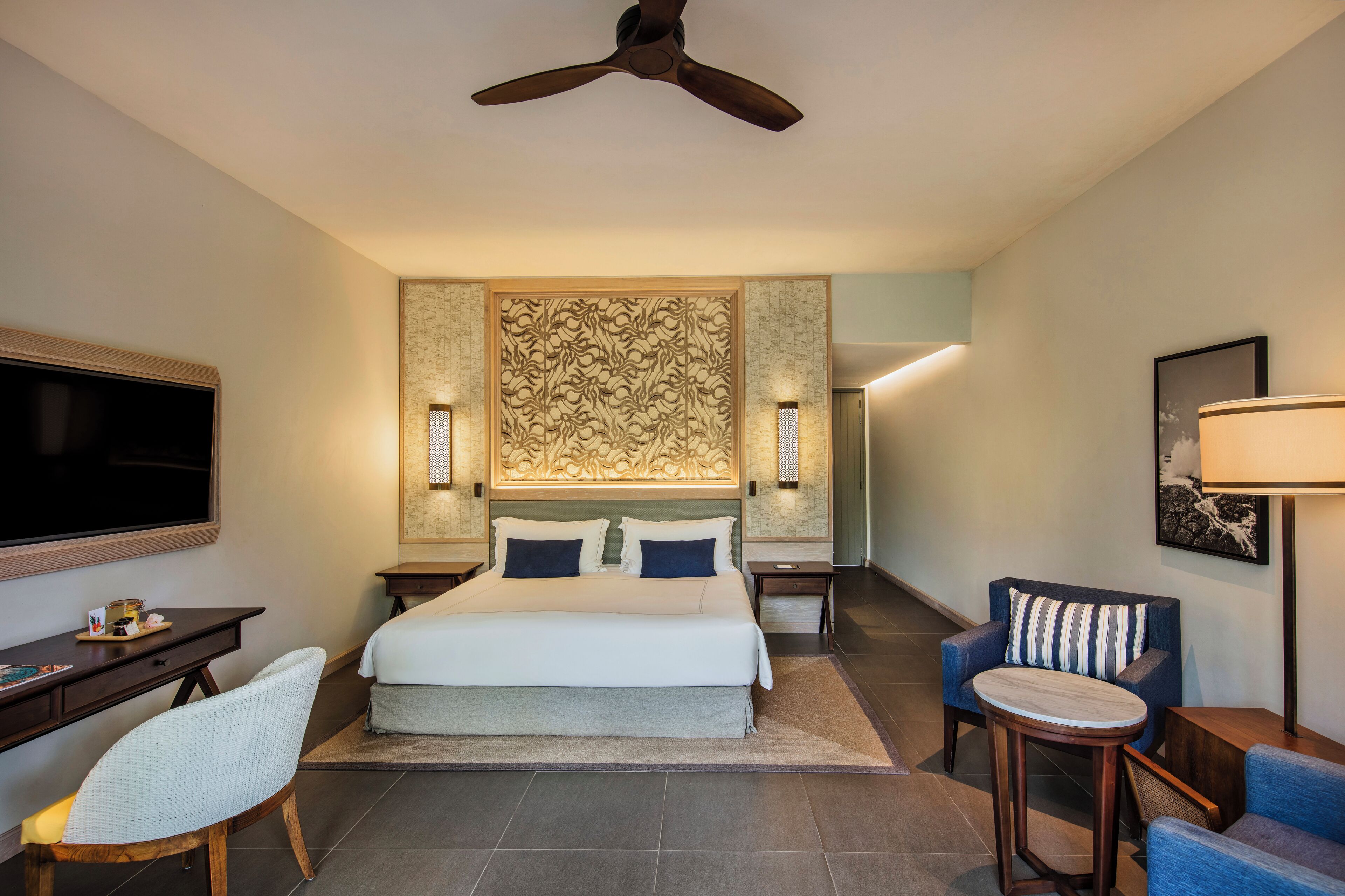 Una habitación de hotel con cama, escritorio, silla, televisión y ventilador de techo.