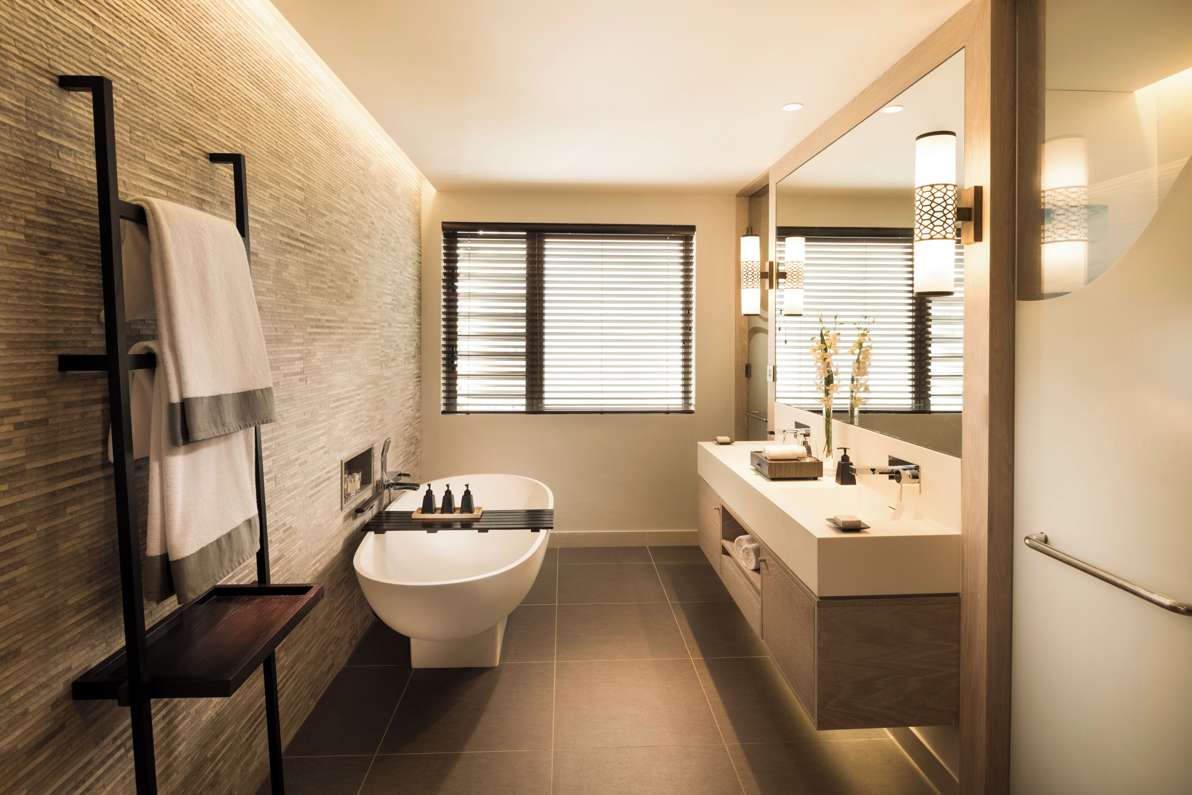 A modern bathroom with a freestanding bathtub, a vanity with a mirror, and a window with blinds.