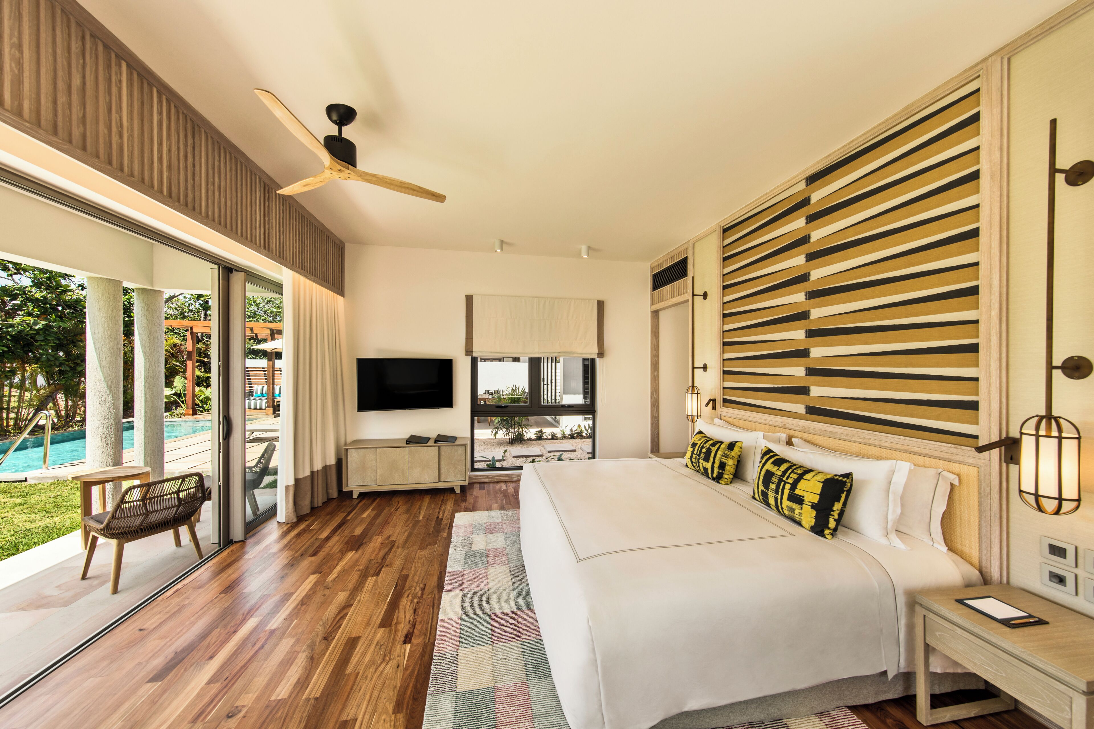 Un dormitorio moderno con una cama grande, ventilador de techo, televisor y vistas a una piscina.