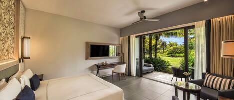 A modern hotel room with a large bed, a desk, a TV, and a balcony with a view of the garden.