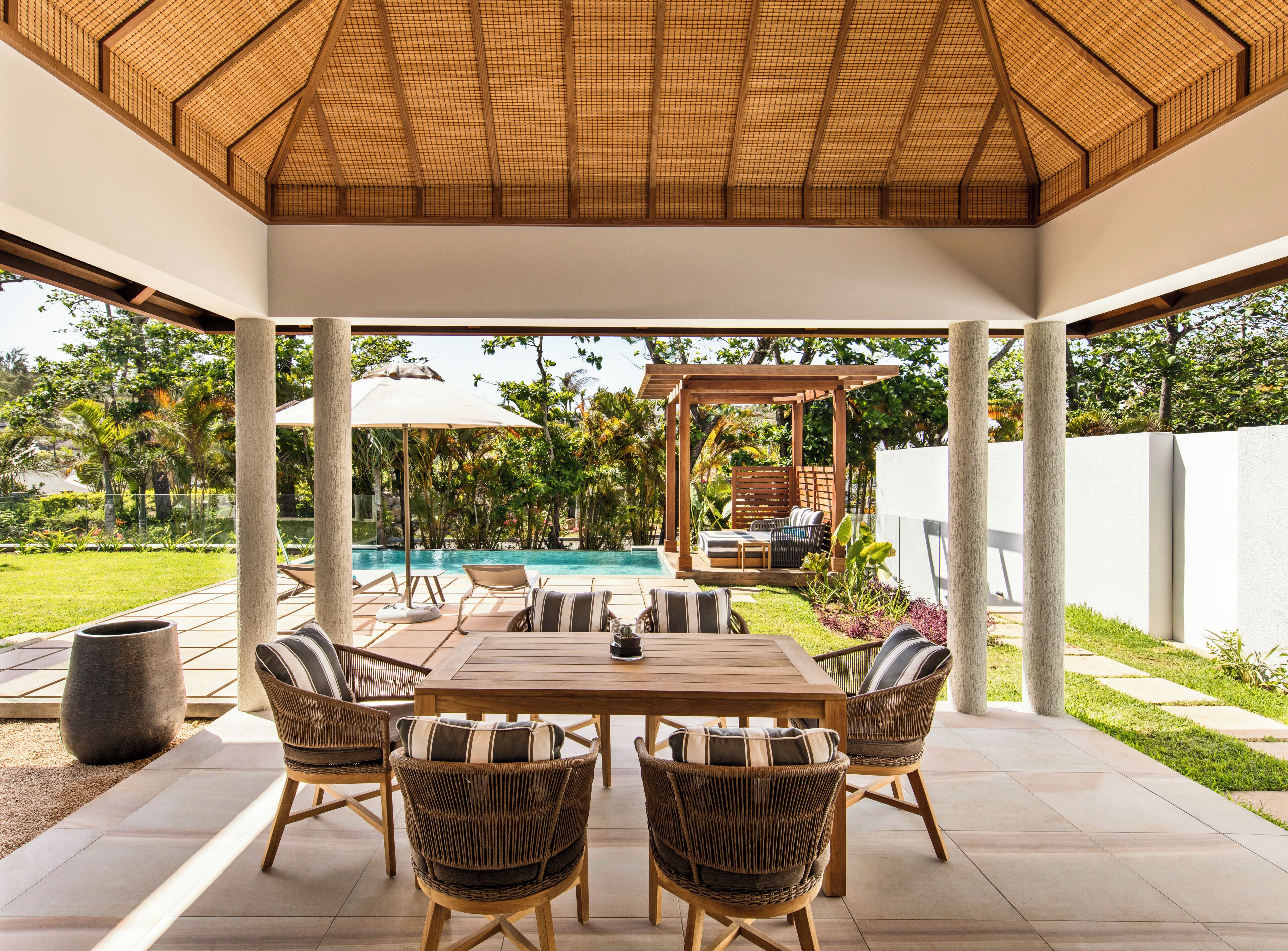 An outdoor patio with a pool, wooden furniture, and a pergola.