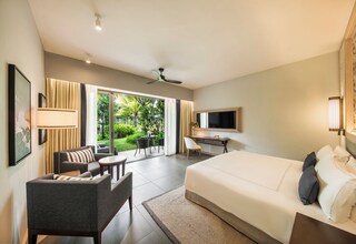A hotel room with a bed, a desk, a chair, a TV, and a view of a garden.
