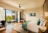A modern bedroom with a large bed, a seating area with a chair, a small table, and a view of the outdoors.
